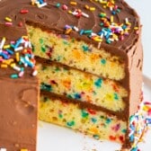 birthday cake on a white plate with chocolate frosting and sprinkles on top.
